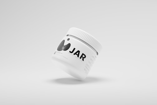 A minimalistic white jar is prominently displayed against a plain light background. The jar has a simple, modern design with black text and abstract graphics. It includes a screw-on lid, and the label appears to be a mockup template with placeholder text.