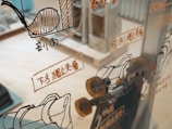 A glass surface reflects various technical schematics and illustrations, likely related to machinery or engineering, with accompanying text in a foreign language. The background shows a blurred interior space, possibly a workshop or an office.