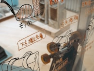 A glass surface reflects various technical schematics and illustrations, likely related to machinery or engineering, with accompanying text in a foreign language. The background shows a blurred interior space, possibly a workshop or an office.
