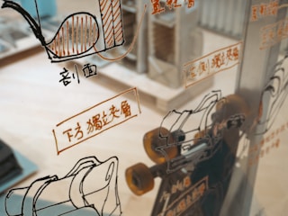 A glass surface reflects various technical schematics and illustrations, likely related to machinery or engineering, with accompanying text in a foreign language. The background shows a blurred interior space, possibly a workshop or an office.