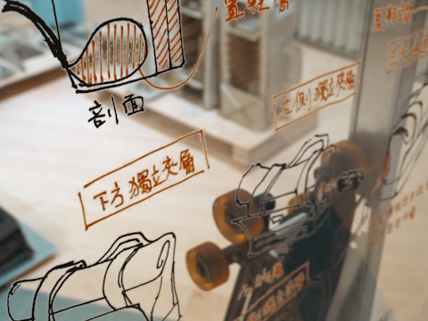A glass surface reflects various technical schematics and illustrations, likely related to machinery or engineering, with accompanying text in a foreign language. The background shows a blurred interior space, possibly a workshop or an office.