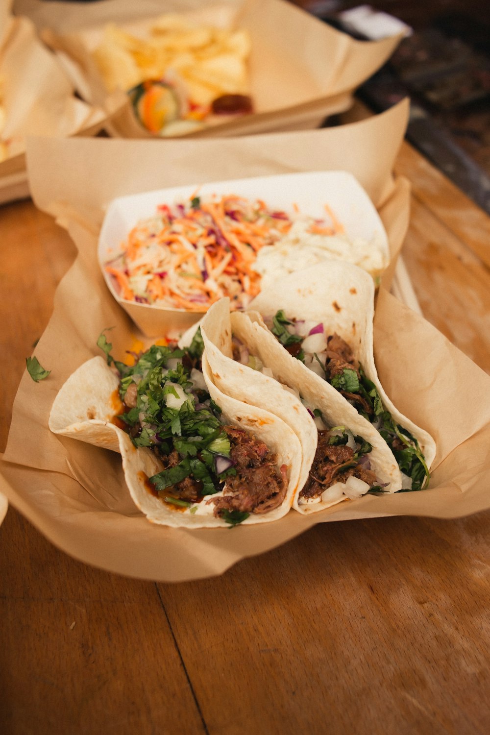 a wooden table topped with three tacos and a bowl of cole slaw