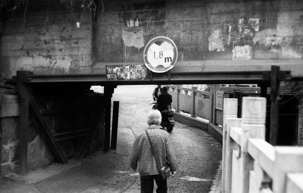 a black and white photo of a person walking under a bridge