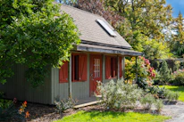 A cozy granny flat with large windows and warm wooden accents nestled in a garden.