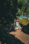 Entrance to the guesthouse with a sandy path, surrounded by greenery and soft sunlight.