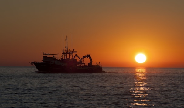 A sunset view over the ocean with a silhouette of a sportfishing boat on the horizon.