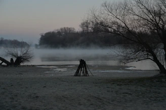 A quiet riverside scene at dawn, with mist rising and a single figure seated in meditation.