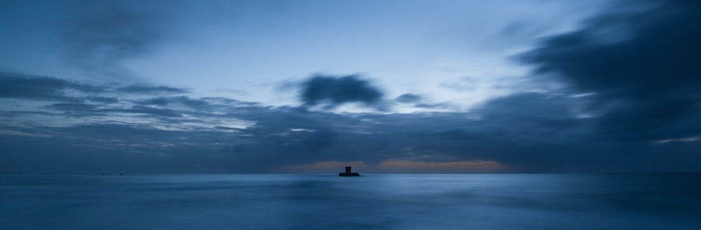 a lighthouse in the middle of the ocean under a cloudy sky