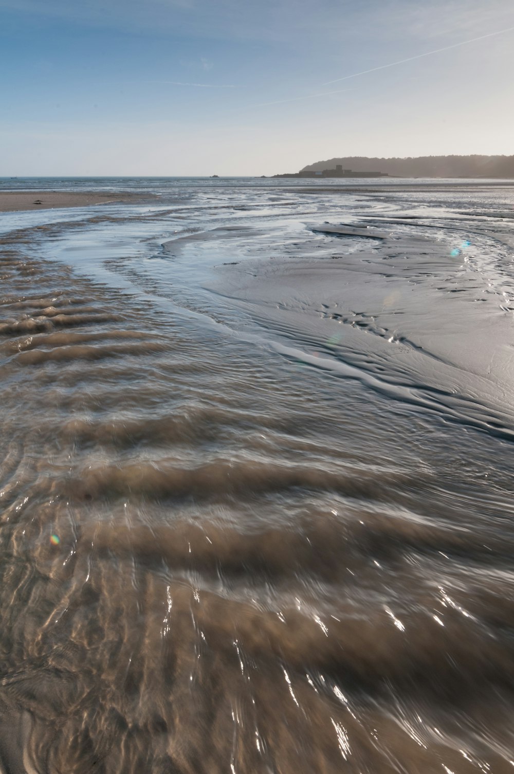 a sandy beach covered in waves under a blue sky