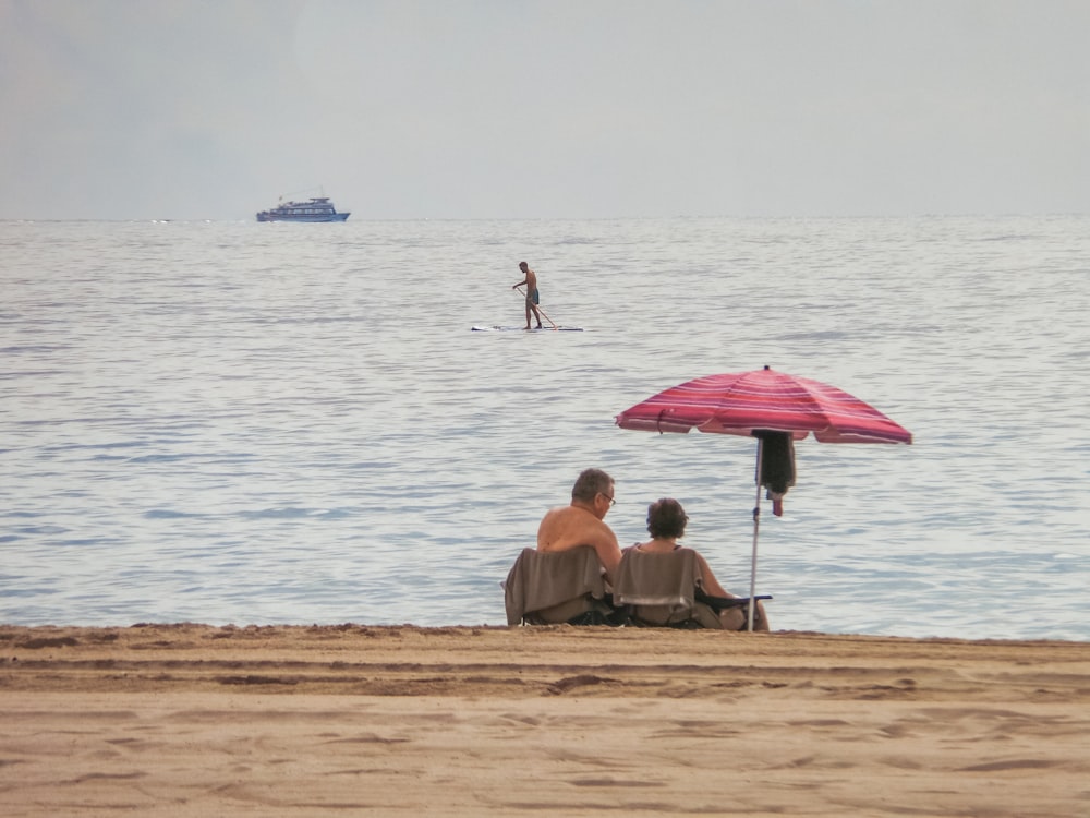 a couple of people sitting on top of a sandy beach