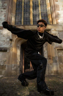 Model in oversized obsidian hoodie with dropped shoulders, standing against brutalist concrete architecture at dusk.