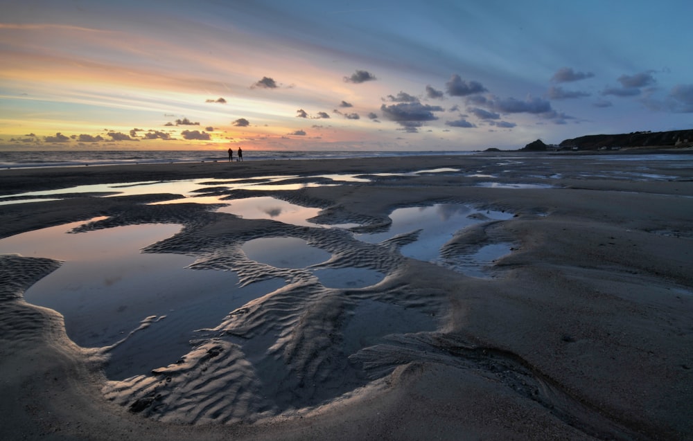 a couple of people standing on top of a sandy beach