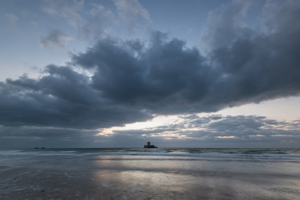 a beach with a boat in the distance under a cloudy sky