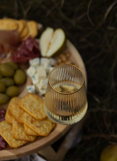 A luxurious spread of olives, pickles, and gourmet crackers beside a glass of red wine.