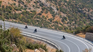 A group of motorbikers navigating a winding Himalayan road surrounded by rocky terrain