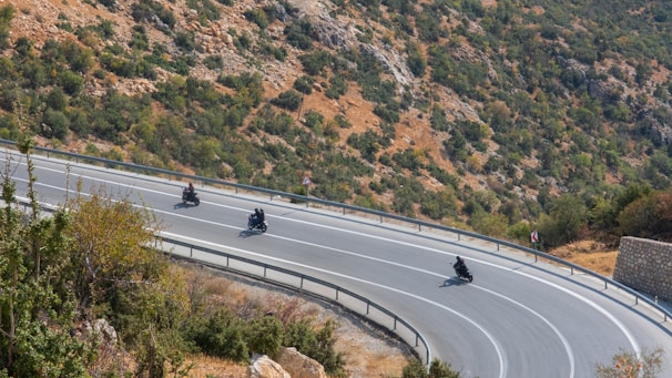 A group of motorbikers navigating a winding Himalayan road surrounded by rocky terrain