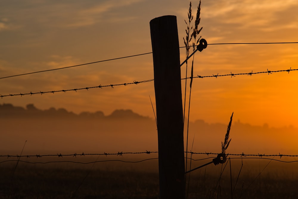 the sun is setting behind a barbed wire fence