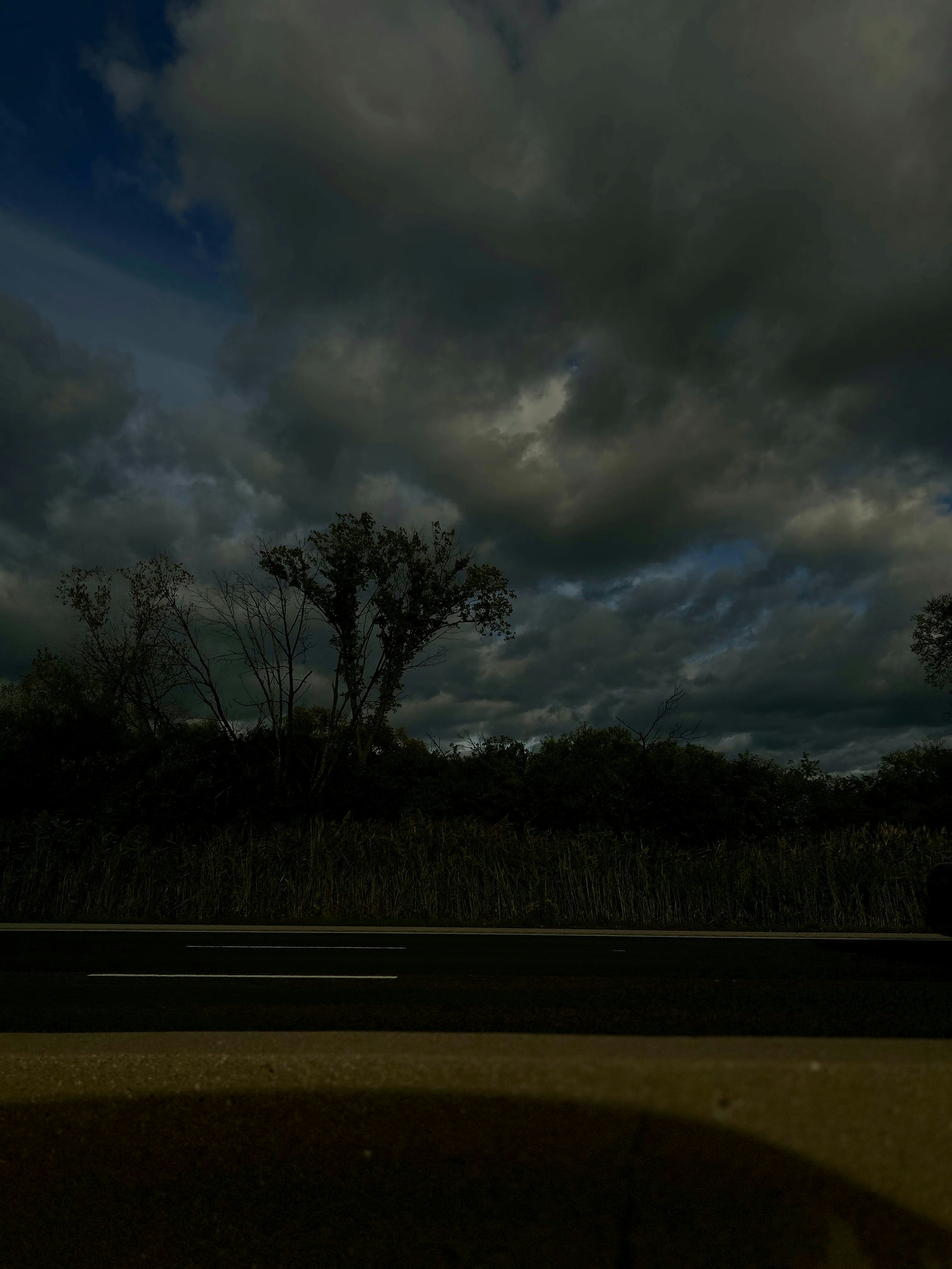 Dark moody country road at dusk with storm clouds, deep blue shadows, lone figure silhouette