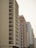 A row of high-rise residential buildings with multiple balconies and windows. The architecture features geometrical patterns, with one building having arches on the facade. The structures have varying colors, including beige, red, and white. The sky appears clear and the trees are visible at the bottom of the image.