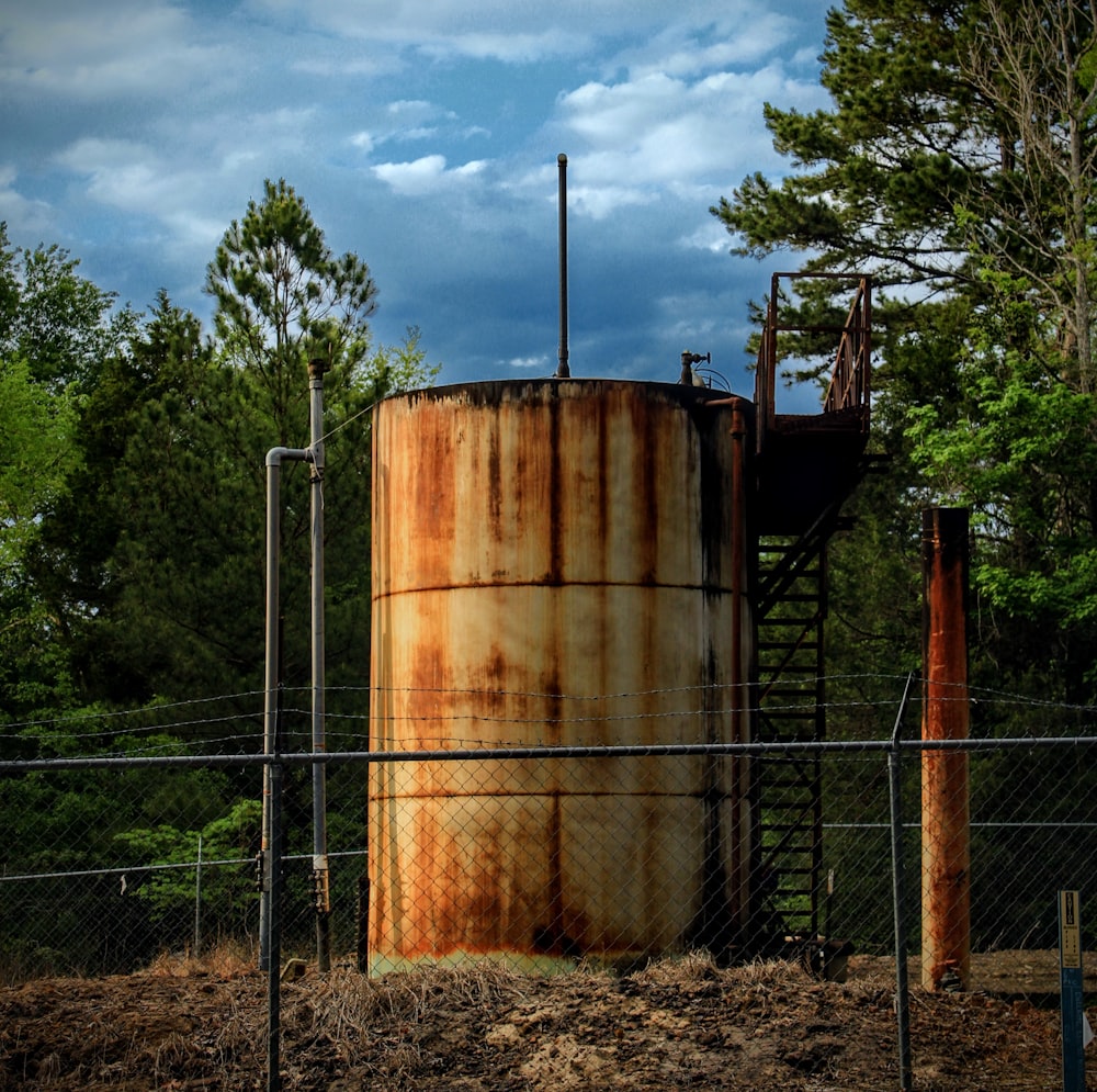 a rusted water tank behind a chain link fence