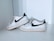 A pair of well-worn, white sneakers with a black swoosh logo displayed on a light gray surface. The shoes have visible signs of wear and dirt, especially on the soles and around the toe area. The laces are loosely tied, and the sneakers are positioned in a casual arrangement.