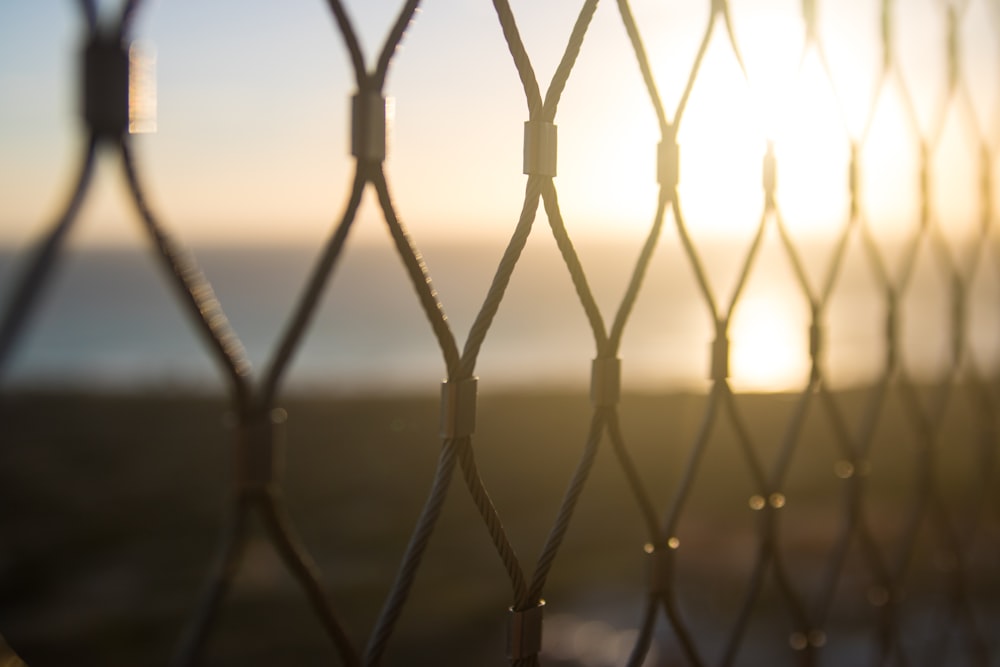 the sun is setting behind a chain link fence