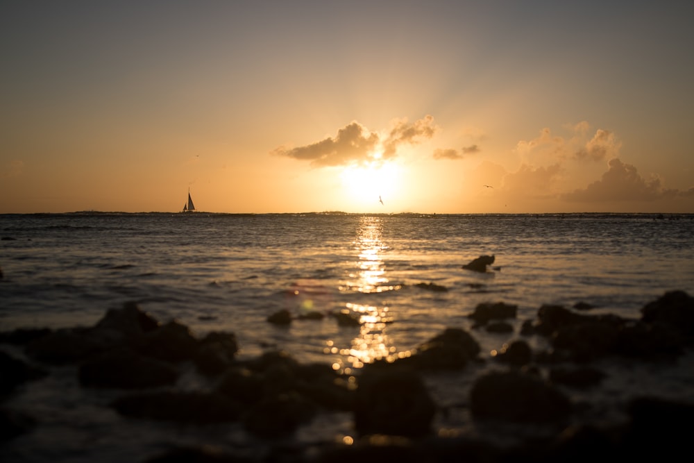 the sun is setting over the ocean with rocks in the foreground