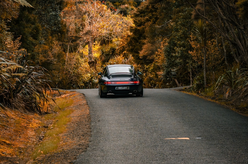 a black car driving down a road surrounded by trees