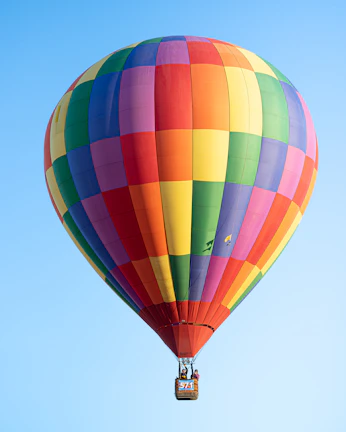 Passengers smiling inside a hot air balloon basket as it soars above a scenic river