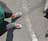 A pair of legs is visible wearing mismatched, colorful sneakers with multicolored checkered patterns and vibrant socks, one red and one green. The person is standing on a rough, textured asphalt road with a faded white line running across.