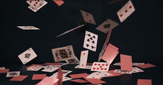 A deck of playing cards scattered mid-air against a dark background, showing various suits and numbers. The cards are dynamically floating, with some already on the surface, creating a sense of motion.