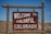 A wooden sign displaying the words 'Welcome to Colorful Colorado' is seen, set against a backdrop of barren hills and a clear blue sky.