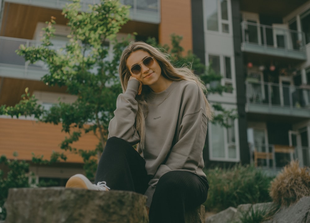 a woman sitting on a rock in front of a building