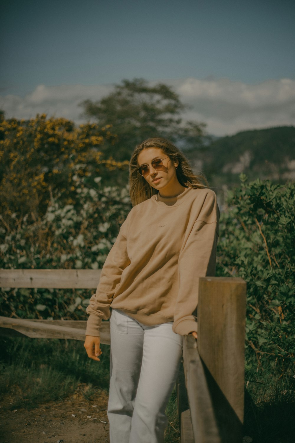 a woman wearing a tan sweater and white pants