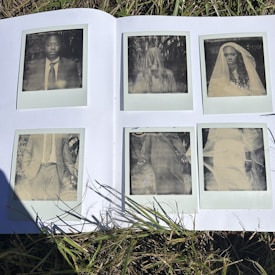 A collection of six vintage-style Polaroid photographs is displayed on an open white book laying on grass. The images capture a man in a suit, a person with long hair obscured by fabric, and two individuals wearing veils, evoking a nostalgic or ethereal mood.