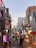 A bustling city street scene with numerous signs written in Korean, displaying a mix of bright neon lights and shopfronts. People are walking along the street, suggesting a lively atmosphere. Buildings of different heights line both sides of the street, indicating an urban setting during early evening.