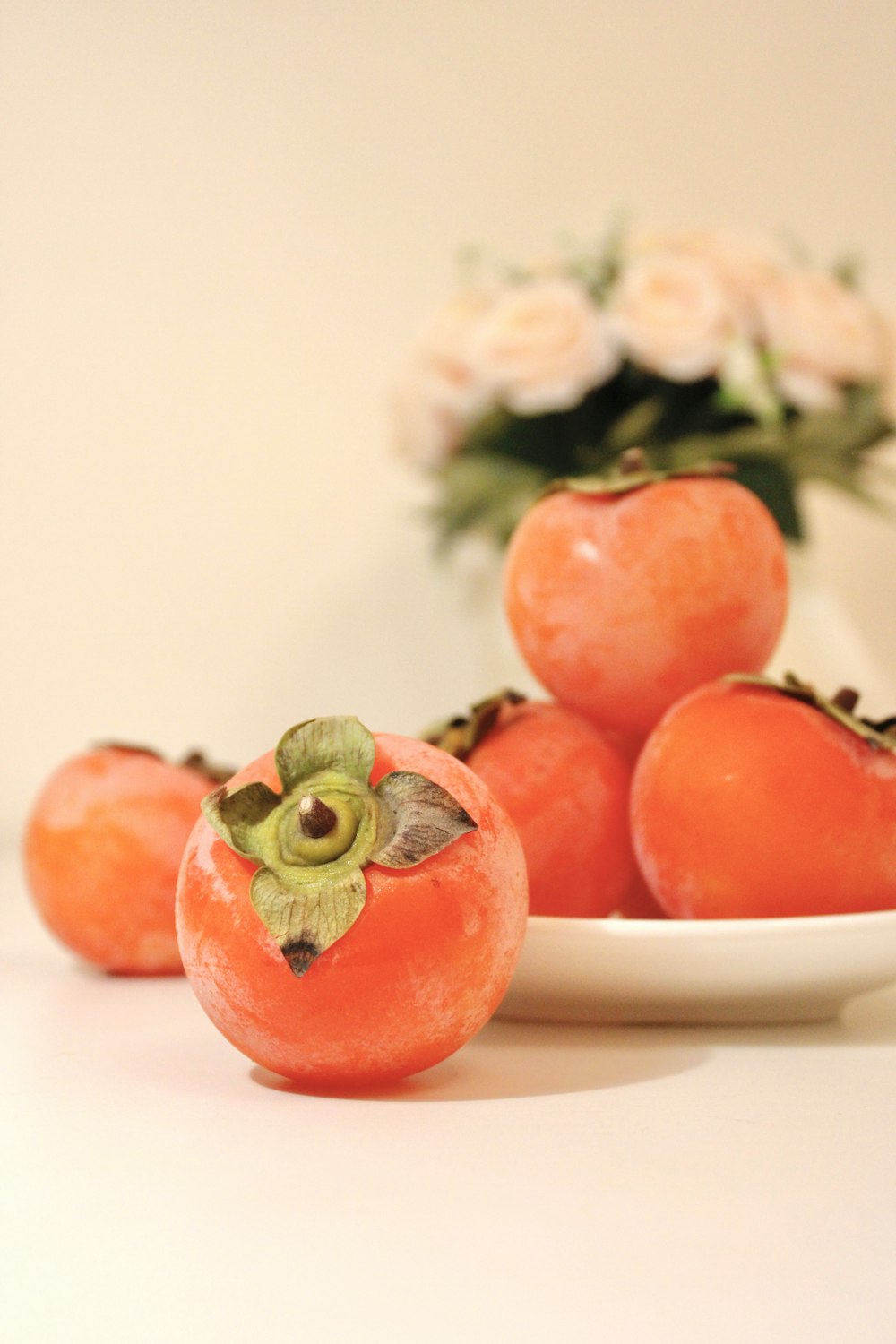 Un plato blanco cubierto con tomates junto a un jarrón de flores