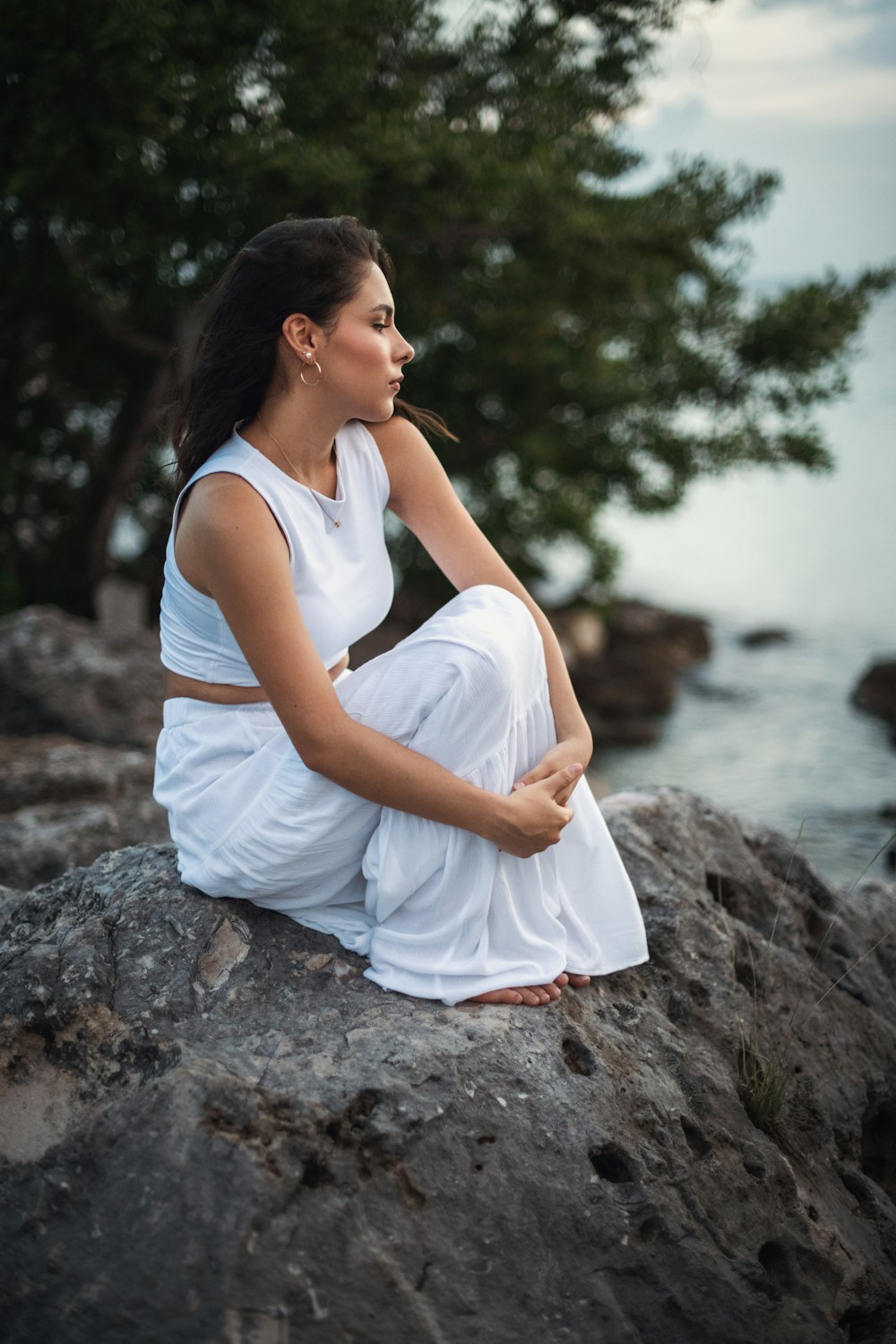 a woman sitting on top of a rock next to a body of water