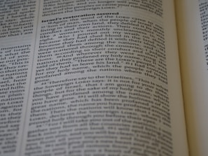 A close-up of an open book displaying text on two pages with headings and paragraphs. The text appears to be religious or scriptural in nature, with verses and structured formatting.