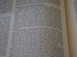 A close-up of an open book displaying text on two pages with headings and paragraphs. The text appears to be religious or scriptural in nature, with verses and structured formatting.