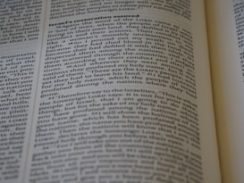 A close-up of an open book displaying text on two pages with headings and paragraphs. The text appears to be religious or scriptural in nature, with verses and structured formatting.