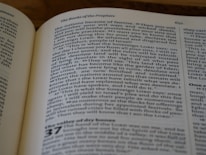 A close-up photograph of an open book, specifically displaying text from a religious or philosophical text. The page features a section titled 'The Books of the Prophets' and includes numbered verses. The text is in a serif font, with some words in small capitals to denote emphasis.
