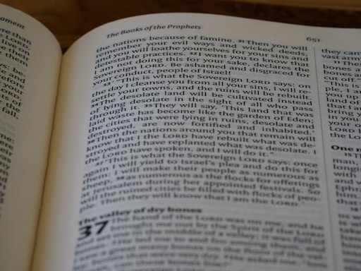 A close-up photograph of an open book, specifically displaying text from a religious or philosophical text. The page features a section titled 'The Books of the Prophets' and includes numbered verses. The text is in a serif font, with some words in small capitals to denote emphasis.