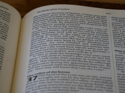 A close-up photograph of an open book, specifically displaying text from a religious or philosophical text. The page features a section titled 'The Books of the Prophets' and includes numbered verses. The text is in a serif font, with some words in small capitals to denote emphasis.