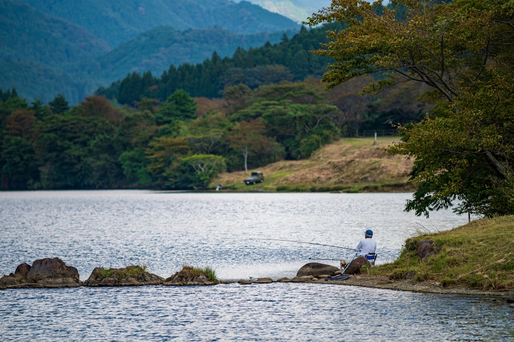 um homem pescando em um lago com montanhas ao fundo