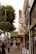 A busy urban street lined with various shops and restaurants, featuring several storefront signs including 'Fillmore Billiards' and 'Wise Sons'. People walk along the sidewalk, some carrying bags and others looking at their phones. There are tall trees on the left side, providing greenery amidst the city setting.