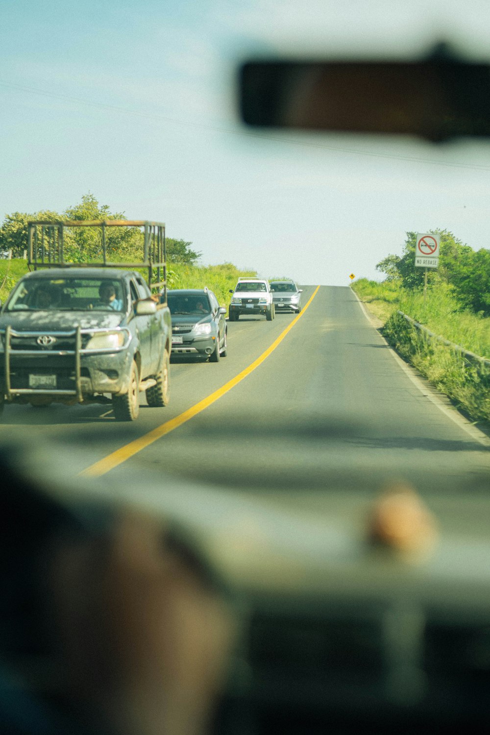 a group of cars driving down a road next to a lush green field