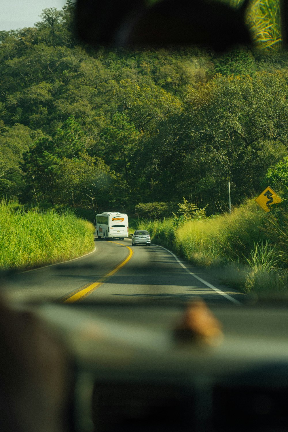 a car driving down a road next to a lush green hillside