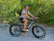 A smiling rider in full gear sitting on a sleek Voltrider electric dirt bike against a forest trail backdrop.