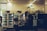 A dimly lit indoor space with two refrigerated display units containing various packaged goods. A large leafy plant decorates the area between the refrigerators. In the foreground, a counter with kitchen appliances and bottles is visible. The setting appears to be a self-service or small convenience area with a calm ambiance.